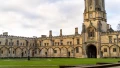 Historic building with intricate architecture, a tall clock tower, and a lush green courtyard, typical of UK landmarks.