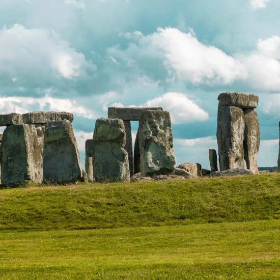 Stonehenge stands majestically under a blue sky, surrounded by green grass and distant fields, showcasing its ancient mystery.