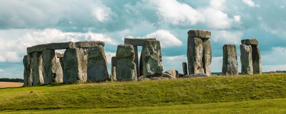 Stonehenge stands majestically under a blue sky, surrounded by green grass and distant fields, showcasing its ancient mystery.