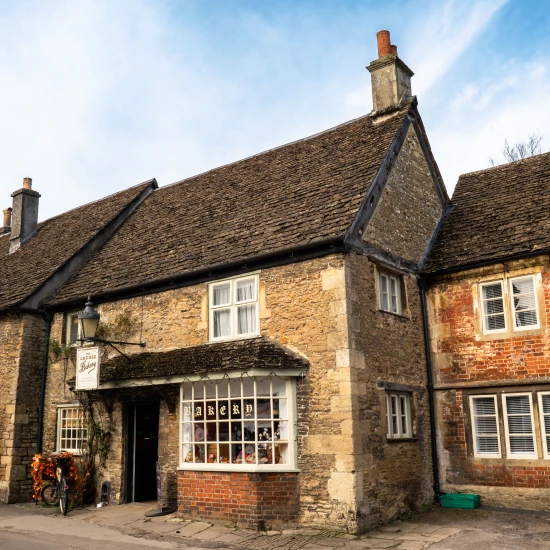 Charming stone and brick cottages line a picturesque street under a clear blue sky, showcasing classic British architecture.