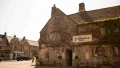 Historic Cotswold Arms pub with ivy-covered stone exterior and cozy outdoor seating, set in a quaint village street.