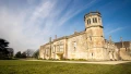 Historic stone building with a distinctive tower set against a clear blue sky and green lawns, ideal for tours in the UK.