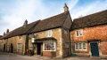 Charming stone and brick cottages line a picturesque street under a clear blue sky, showcasing classic British architecture.