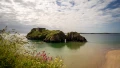 A scenic coastal view featuring a rocky island with a ruined structure, surrounded by calm waters and lush green landscape.
