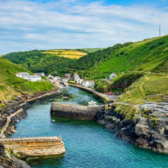 Lush green hills surround a quaint coastal village, with a winding river and rocky shoreline, ideal for exploration.