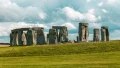 Stonehenge stands majestically on the green landscape, under a dramatic sky with scattered clouds. A testament to ancient history.