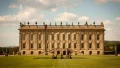The grand facade of Chatsworth House features ornate architecture and sculptures, surrounded by lush green gardens.