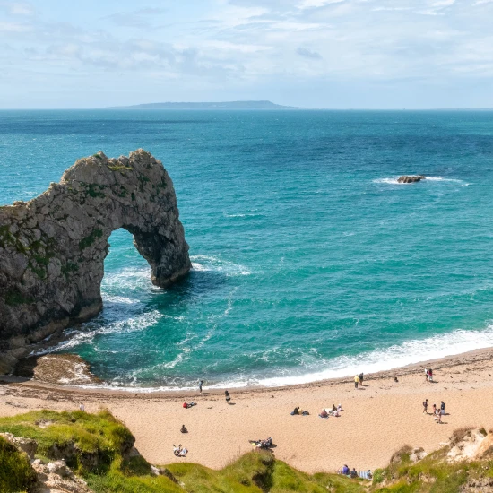 A scenic view of Durdle Door, featuring cliffs, a sandy beach, and visitors enjoying the picturesque coastal landscape.