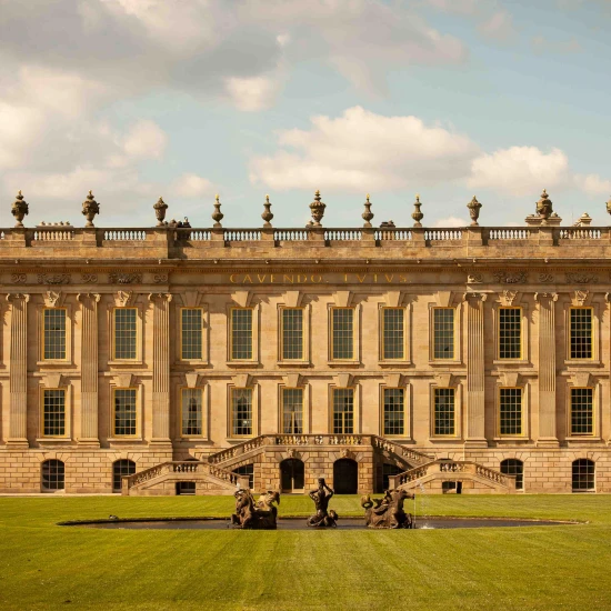 The grand exterior of Chatsworth House showcases its stunning architecture and manicured gardens under a clear blue sky.