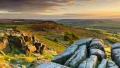 A stunning landscape with rugged rocks and rolling hills, illuminated by a golden sunset, showcasing the beauty of the UK.
