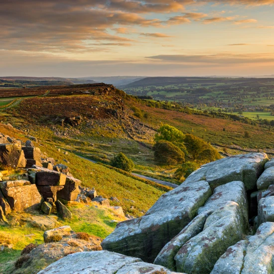 A scenic view of rolling hills and rocky outcrops at sunset, showcasing the natural beauty of the UK countryside.