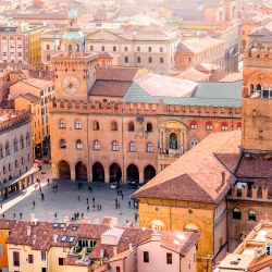 Aerial view of historic buildings with terracotta roofs in a vibrant Italian city square, bustling with visitors and activity.