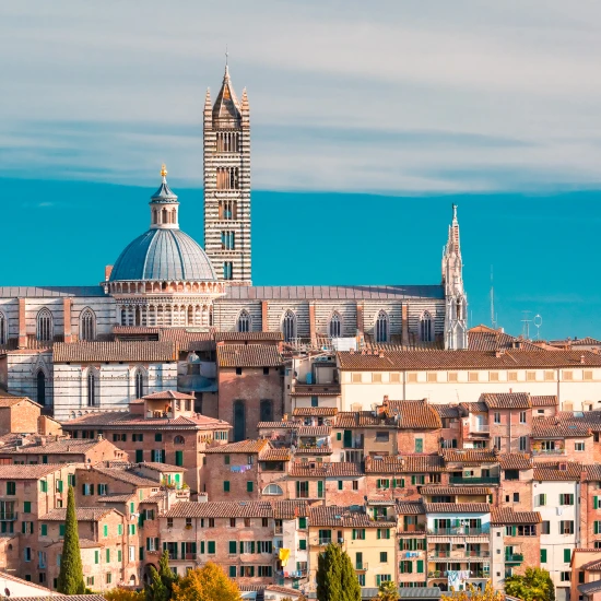 A panoramic view of historic Siena, Italy, featuring its iconic cathedral and medieval architecture against a clear blue sky.