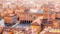 Aerial view of historic buildings with terracotta roofs in a vibrant Italian city square, bustling with visitors and activity.