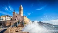 A scenic coastal view featuring a historic church, vibrant sky, and crashing waves against rocky shoreline.