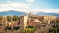 Scenic view of a historic palace and fortress surrounded by lush greenery and mountains under a clear blue sky.