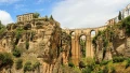 A stunning view of a bridge spanning between high cliffs, framed by lush greenery and quaint buildings above.