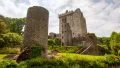 A medieval castle surrounded by lush greenery, showcasing stone towers and gardens, with visitors exploring the grounds.
