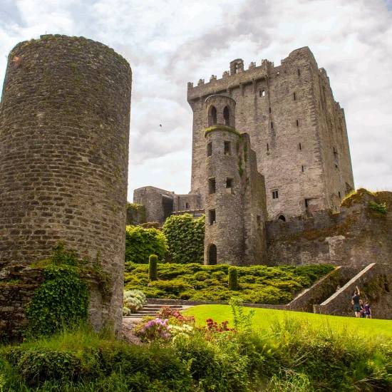 A medieval castle surrounded by lush greenery, showcasing stone towers and gardens, with visitors exploring the grounds.