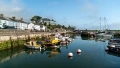 A serene harbor scene featuring colorful boats, calm water, and quaint buildings lining the shore under a clear blue sky.