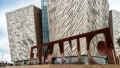 The striking exterior of the Titanic Belfast building with a large, rust-colored installation in front.