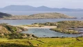 Stunning coastal landscape with green hills, serene waters, and boats anchored near sandy shores under a clear sky.