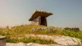 A prehistoric stone monument set on a hillside, surrounded by wildflowers and greenery under a clear sky.