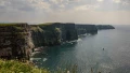 Dramatic cliffs tower over a tranquil sea under a cloudy sky, capturing the beauty of the UK’s natural landscape.