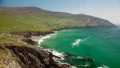 Stunning coastal view of green hills, rocky cliffs, and turquoise waters under a clear sky, perfect for exploring the UK.