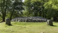 Ancient stone burial cairn surrounded by greenery, with two large standing stones in the foreground and a rocky mound behind.