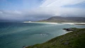 Stunning coastal view with turquoise waters, sandy beaches, and hills under a partly cloudy sky, showcasing the natural beauty of the UK.