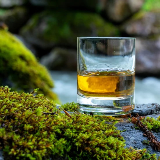 Glass of whisky on a rock by a fast flowing river