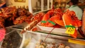 Fresh seafood display featuring lobsters and crabs, bright colors and price tags visible in a bustling market setting.
