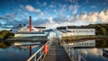 A scenic view of Lagavulin distillery by the water, featuring a wooden pier and a backdrop of clouds and greenery.