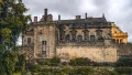 Historic castle with intricate stonework, surrounded by lush gardens under a cloudy sky, representing UK heritage.