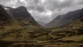 A panoramic view of a dramatic valley surrounded by rugged mountains under a cloudy sky, showcasing Scotland's natural beauty.