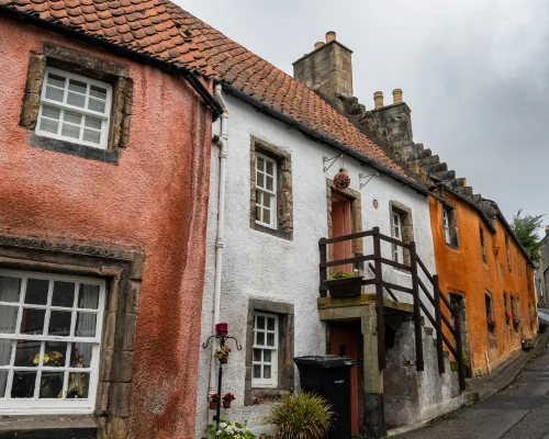 Colorful, quaint houses line a narrow, winding street under a cloudy sky, showcasing the charm of a UK village.