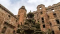 A view of a historic castle's intricate stonework and sculptures, showcasing its architectural details against a cloudy sky.