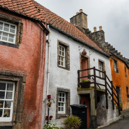 Charming colorful cottages line a narrow street under a cloudy sky, showcasing traditional British architecture.