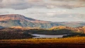 Breathtaking Scottish landscape featuring rolling hills, lush forests, and a serene lake under a cloudy sky.