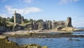 Ruins of a historic stone tower and walls by the coast, surrounded by sandy beach and rocky shoreline under a bright blue sky.