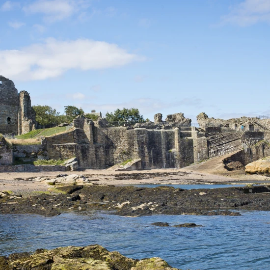 Ruins of a historic stone tower and walls by the coast, surrounded by sandy beach and rocky shoreline under a bright blue sky.