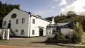 Glengoyne Distillery building with sign, lush greenery, and blue sky, inviting visitors to explore its whisky heritage.
