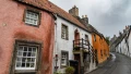 Colorful, quaint houses line a narrow, winding street under a cloudy sky, showcasing the charm of a UK village.