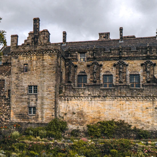 Historic stone castle with intricate details, surrounded by a lush garden and under a cloudy sky. Perfect for small group tours.