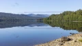 Serene lake reflecting lush green hills under a clear blue sky, offering a peaceful natural escape in the UK.
