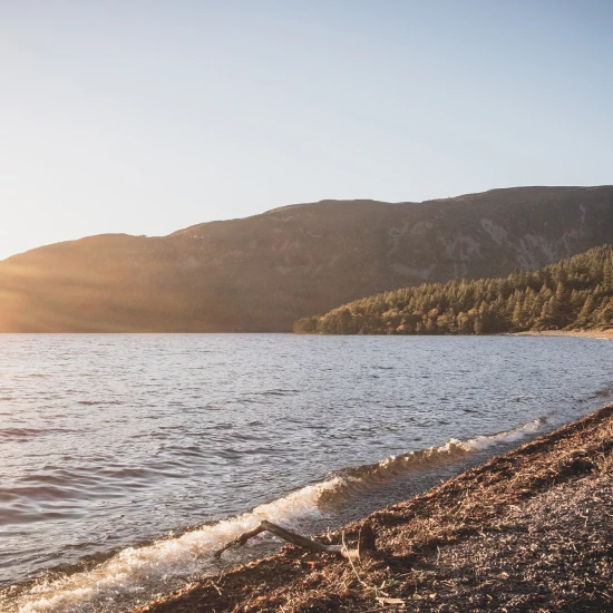 Serene lakeside scene with gentle waves and sunlit hills, perfect for exploring nature on a small group tour.