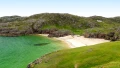 Scenic view of a tranquil beach with sandy shores, turquoise waters, and lush green hills in a picturesque coastal landscape.