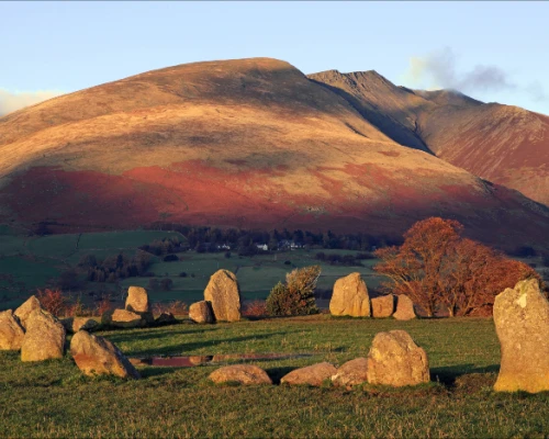 Ancient stone circle against a backdrop of rolling hills under a clear sky, showcasing the beauty of the UK countryside.