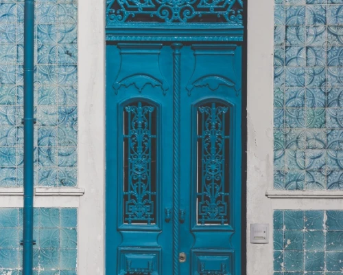 A vibrant blue door with intricate designs, framed by patterned blue tiles on the wall. 